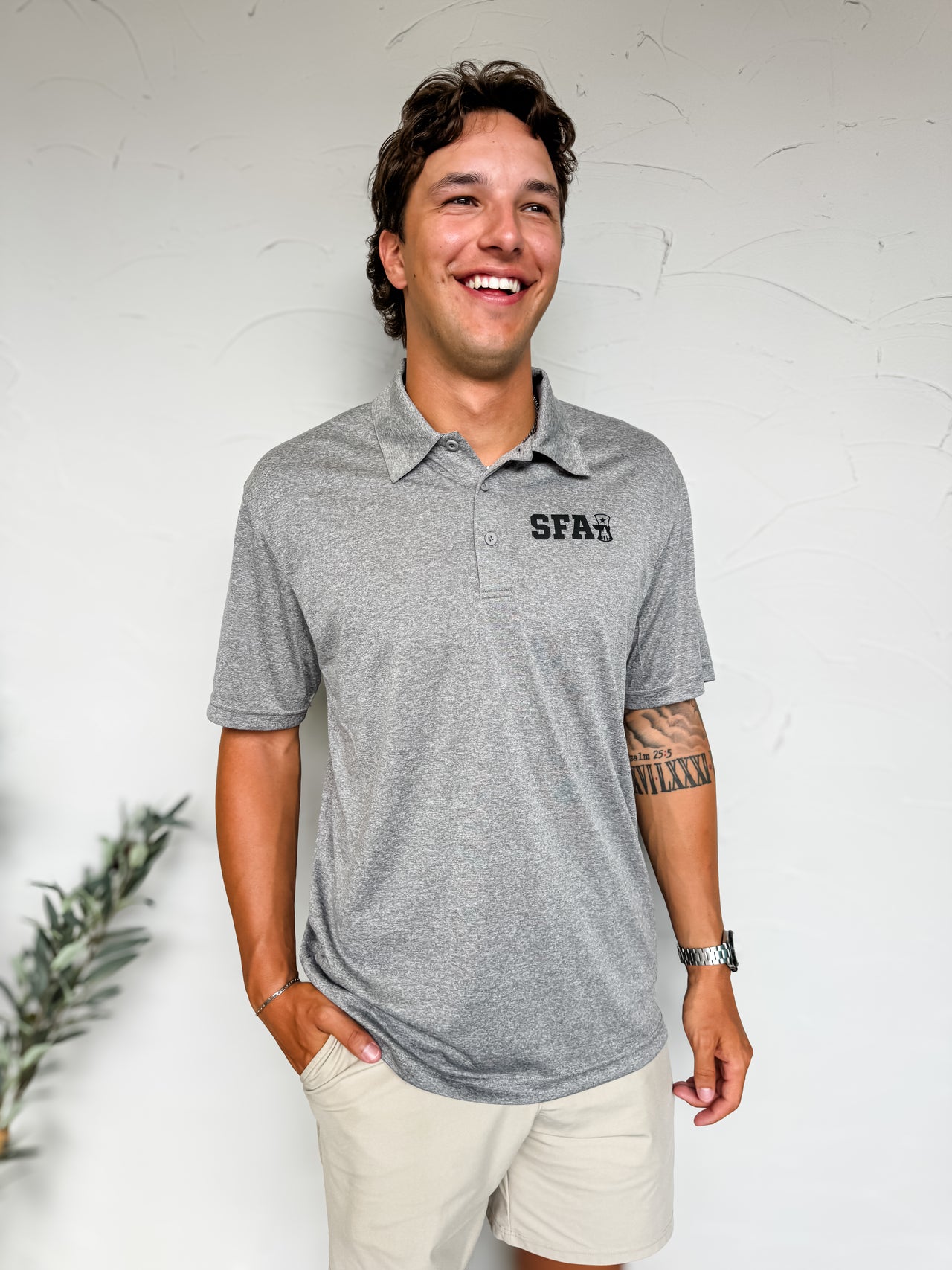 Man wearing a gray polo shirt with 'SFA' logo against a white wall