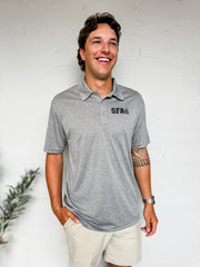 Man wearing a gray polo shirt with 'SFA' logo against a white wall