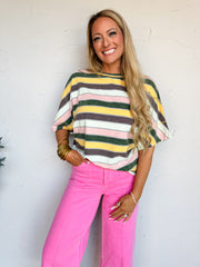Woman wearing a colorful striped sweater and pink pants against a white wall