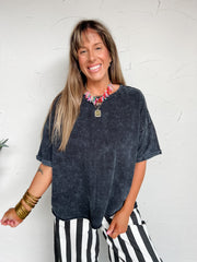 Woman wearing a dark blue oversized shirt and black and white striped pants against a white wall.