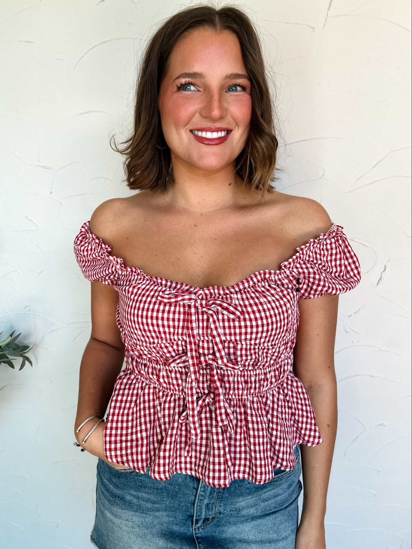 Woman wearing a red and white checkered off-shoulder top against a light background