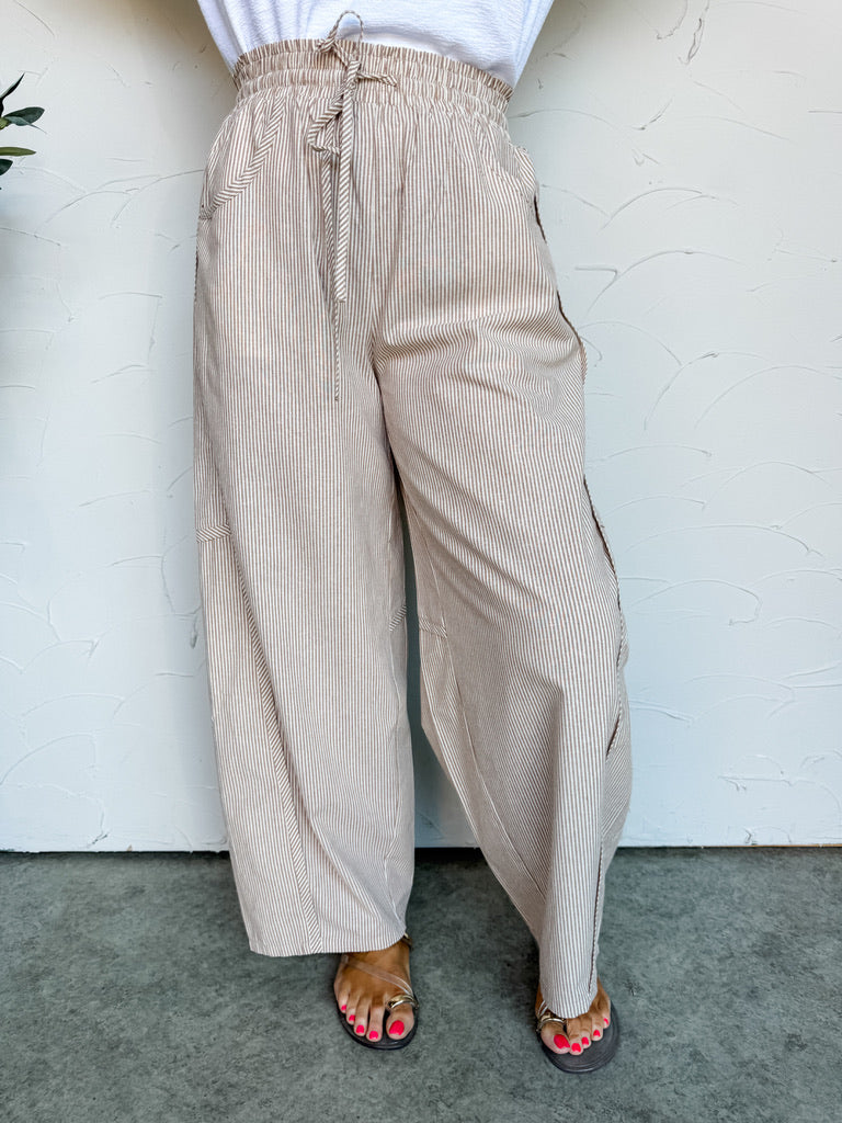 Beige striped pants worn by a person against a white wall.
