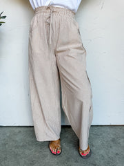 Beige striped pants worn by a person against a white wall.