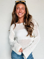 Woman wearing a white mesh knit sweater and denim shorts against a light background