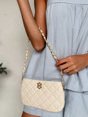 Person wearing a light blue dress and holding a cream-colored quilted handbag with a brand logo.