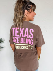 Woman wearing a brown t-shirt with pink text on the back, standing against a white wall.