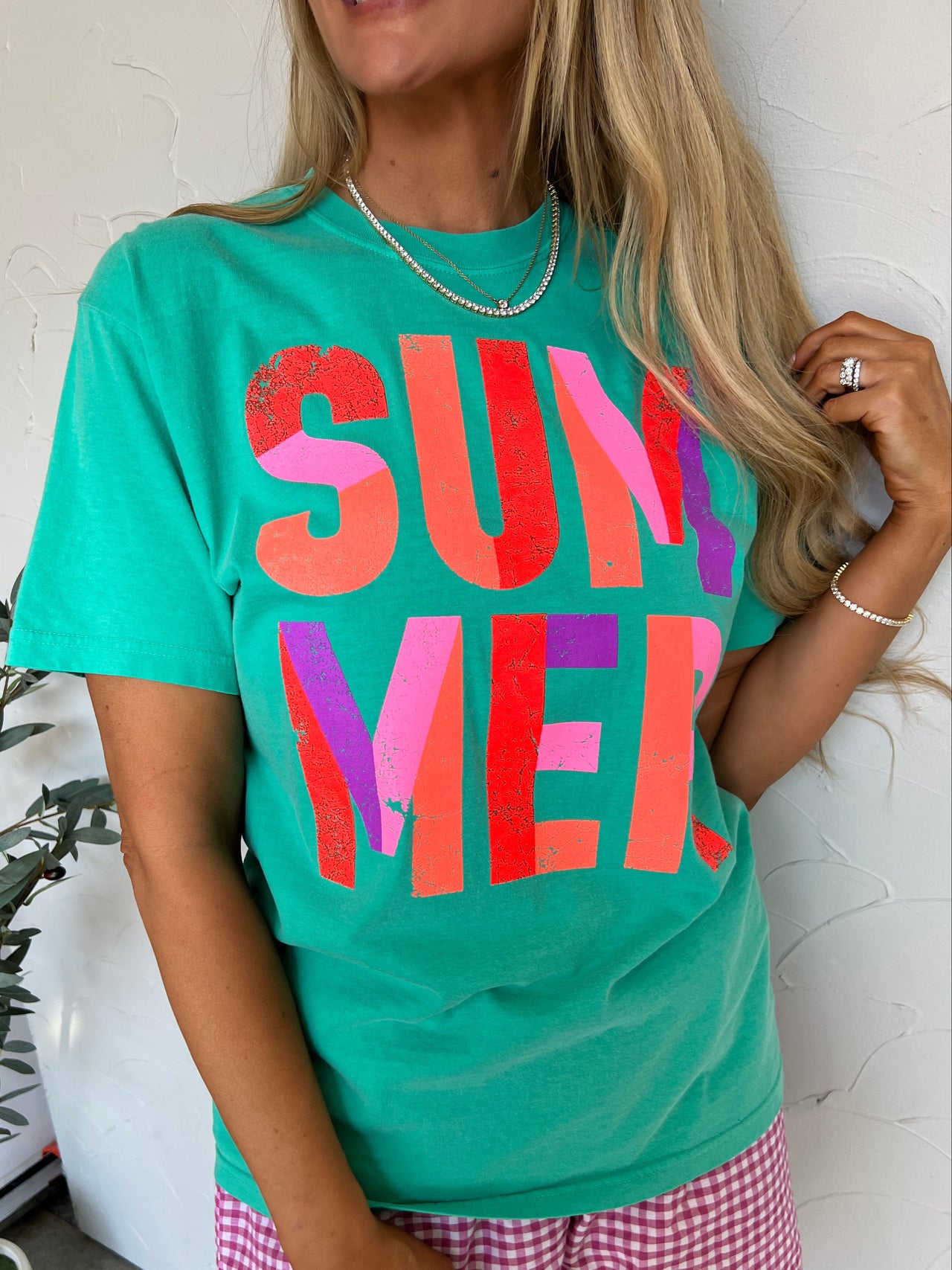 Woman wearing a green 'SUMMER' t-shirt and pink shorts indoors.