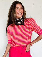 Woman wearing a pink and red striped top with pink pants against a white wall