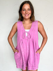 Woman wearing an purple romper with sunglasses against a white background