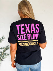 Person wearing a black t-shirt with pink and yellow text against a white wall.