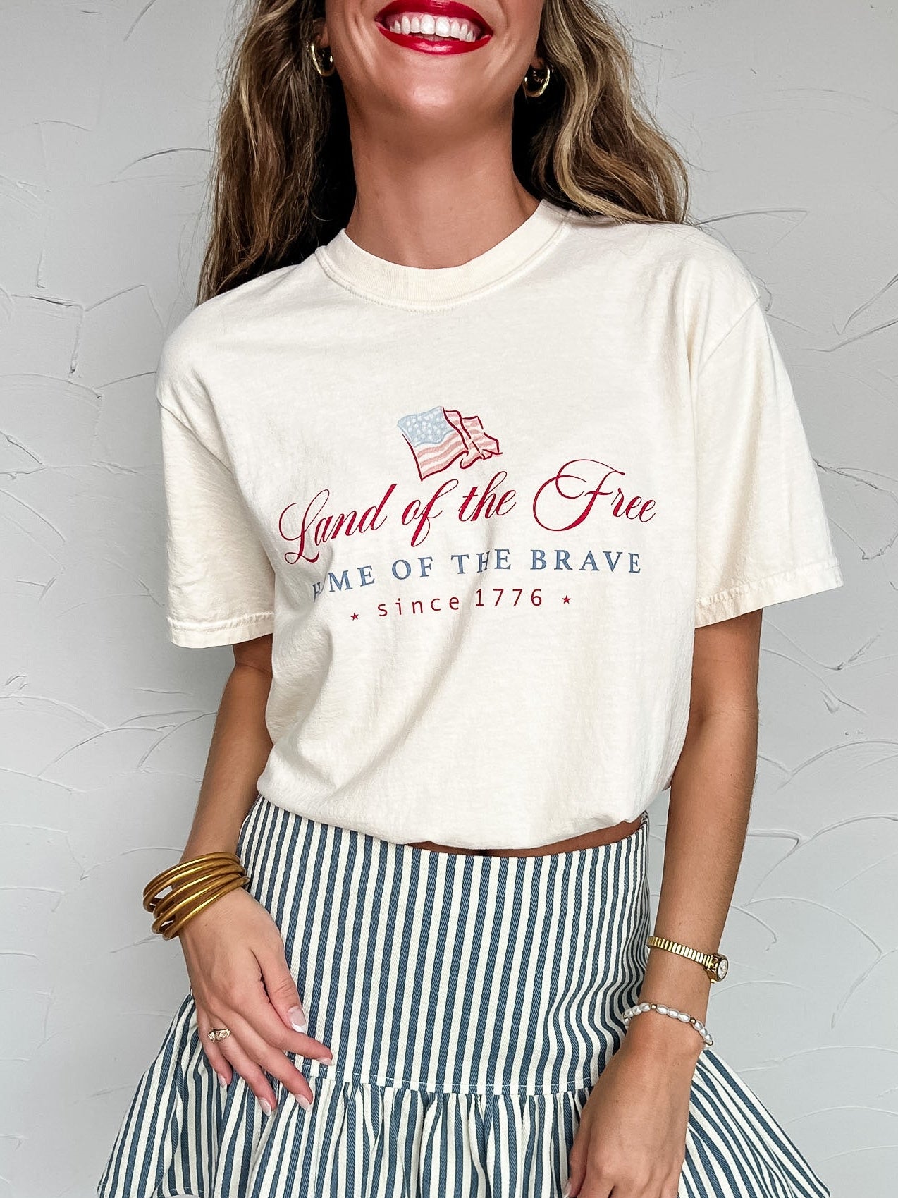 Woman wearing a white t-shirt with a patriotic design and a striped skirt against a plain background