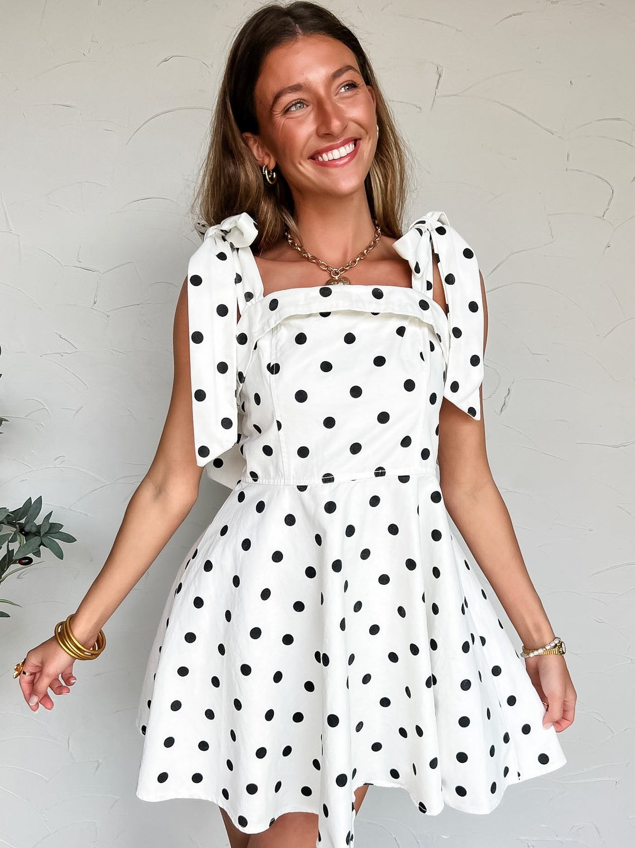 Woman wearing a white dress with black polka dots against a plain background