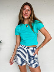 Woman wearing a turquoise top and striped shorts against a white wall
