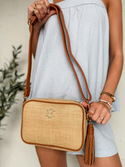 Person holding a woven handbag with a tassel against a neutral background