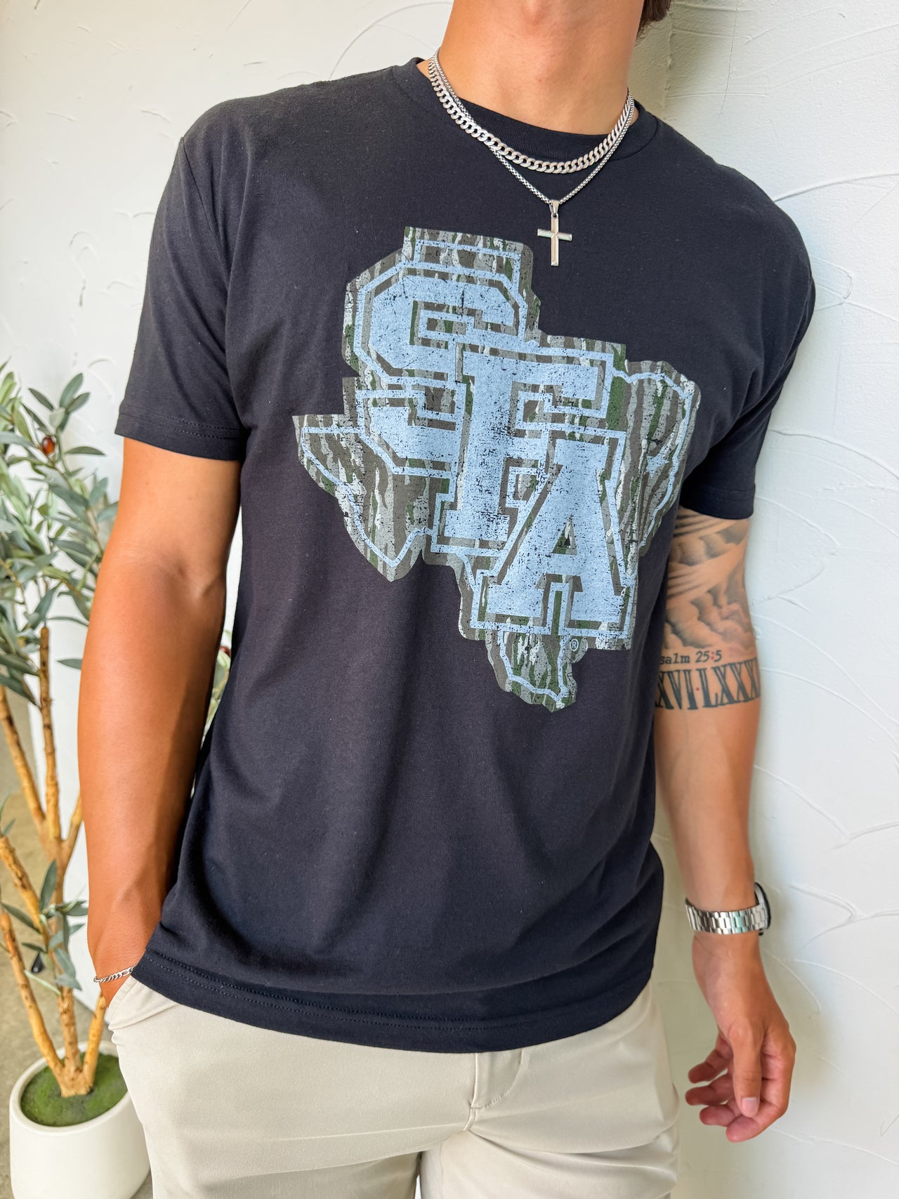 Person wearing a black t-shirt with a blue Texas-shaped graphic design against a white wall.