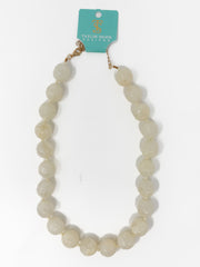 A beaded necklace made of round, polished cream-colored beads with a gold-tone clasp, attached to a teal card that reads 'Taylor Shaye Designs', photographed on a white background.