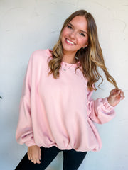 Catie wearing the LovLov Game Changer Cinch Waist Pullover in Vintage Pink, made of 50% cotton and 50% polyester, featuring long sleeves, dropped shoulders, a center-back seam, and a gathered hem, paired with black jeans.⠋