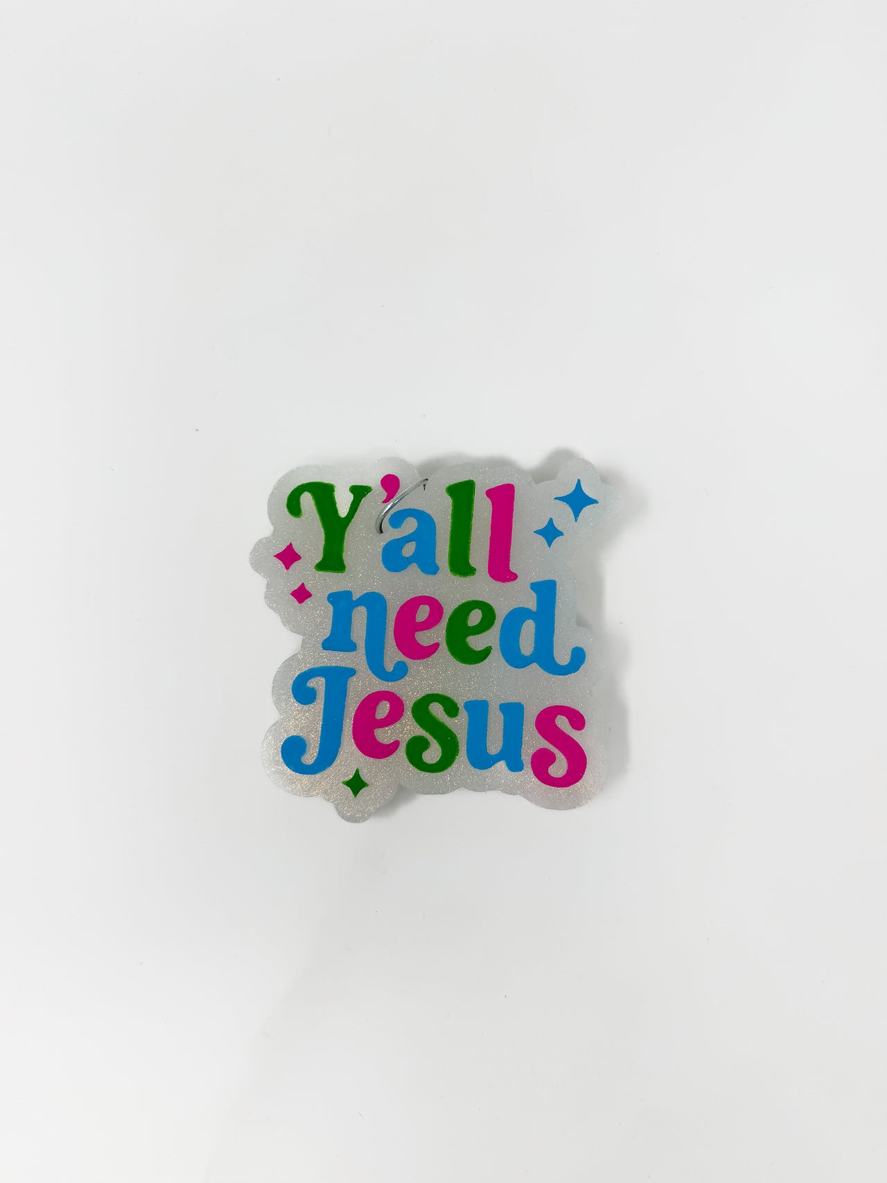 A car air freshener featuring a white glitter background shaped around the words "Y'all need Jesus" in a colorful retro font, shown against a plain white background.