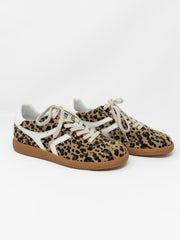 A pair of low-top sneakers featuring a leopard print pattern in beige, brown, and black, with white side stripes, white laces, and brown gum soles, photographed on a clean white background.