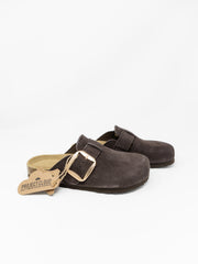 A pair of dark brown suede clogs with gold-tone buckle straps, shown on a clean white background. One clog is positioned in front of the other, with a tan paper tag attached to the front clog's strap that reads 'PROJECT CLOUD'.