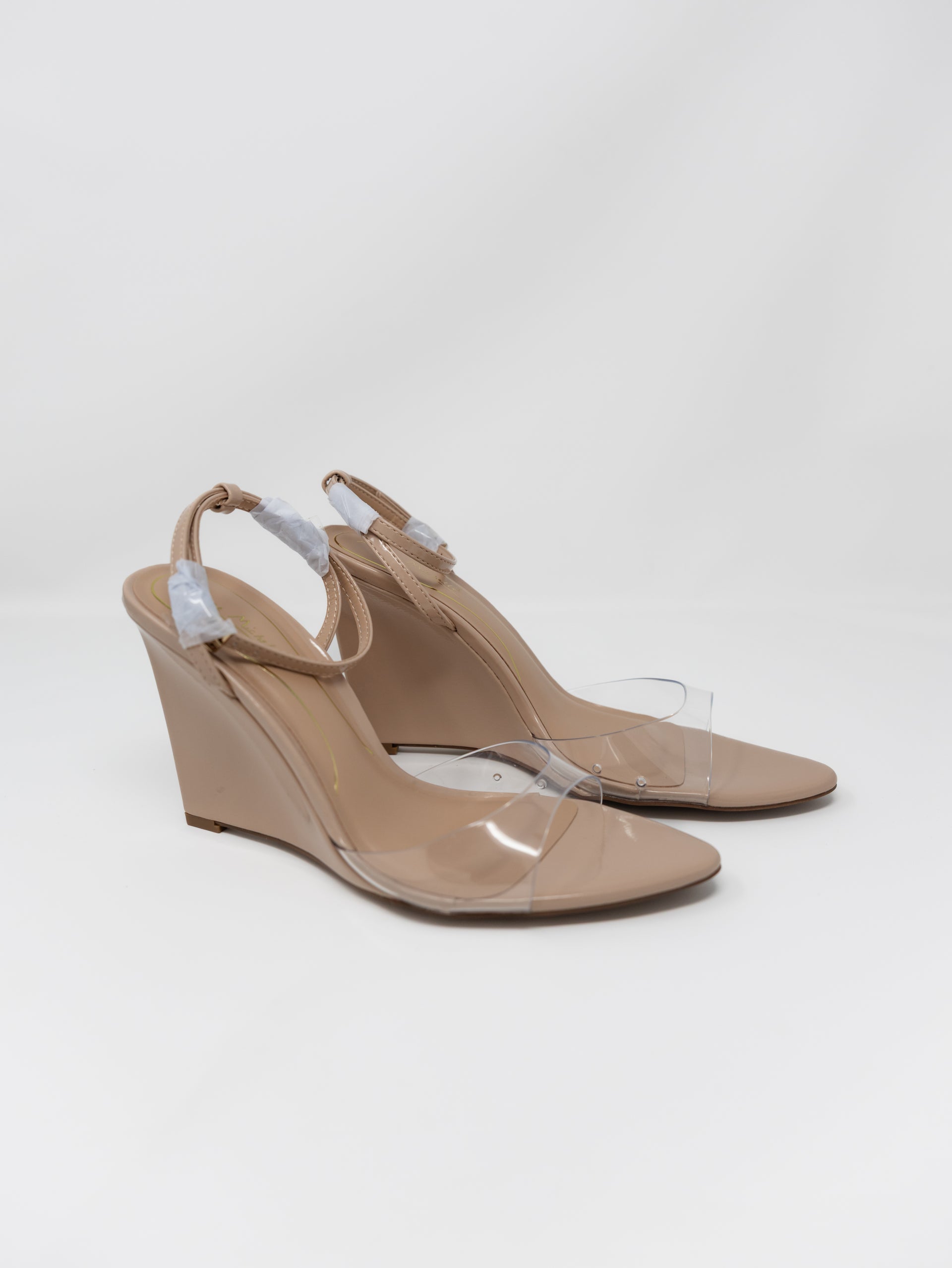 A pair of nude wedge sandals with clear transparent toe straps, shown on a light gray studio background.