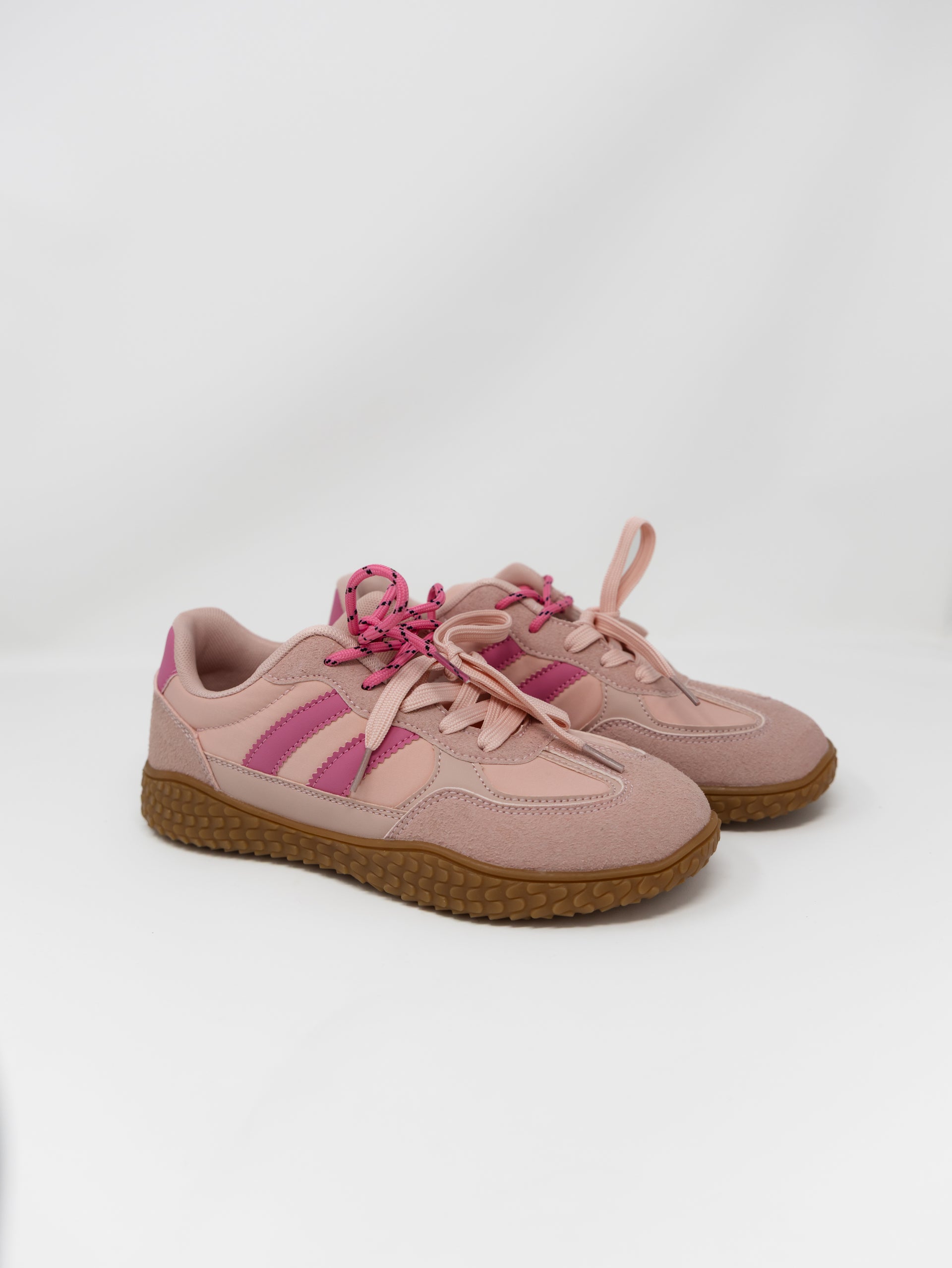 A pair of low-top sneakers in dusty pink suede and mesh, featuring bright pink side stripes, matching pink laces, and brown gum soles, photographed on a light gray studio background.