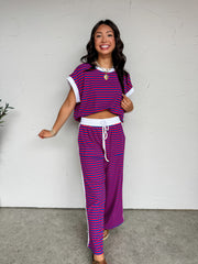 A two-piece casual lounge set featuring a vibrant red and royal blue horizontal stripe pattern, crafted from a soft knit fabric blend of 95% cotton and 5% spandex. The set includes a relaxed-fit, oversized short-sleeve top with a solid white crew neckline and matching white cuffed sleeve borders. The coordinating wide-leg pants feature an elasticized waistband with a functional white drawstring and thin white contrast piping running down the sides.