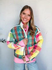 Catie modeling the Something Cute Quilted Patchwork Puffer Jacket by J. NNA, made of 100% polyester, with diamond quilting, a teal and rust plaid back, contrasting pink, yellow, and cream plaid sleeves, and a stand collar, styled with light-wash jeans.
