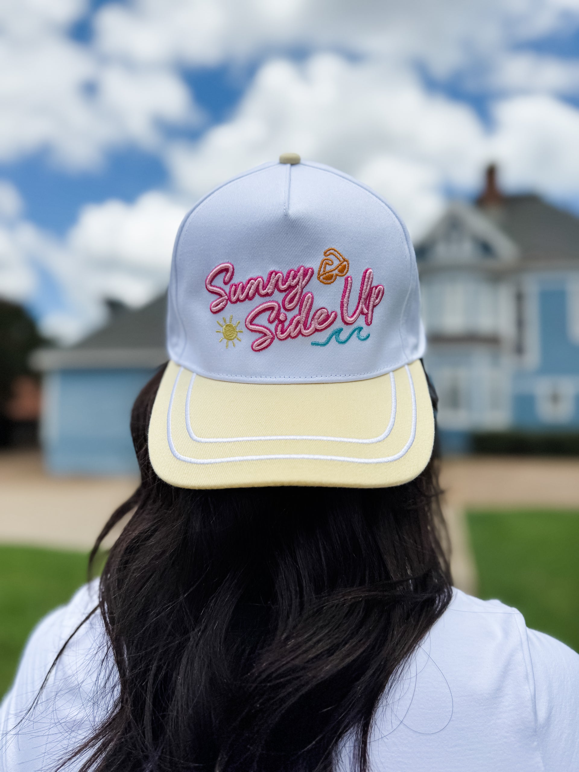 Person wearing a cap with 'Sunny Side Up' text against a blurred outdoor background