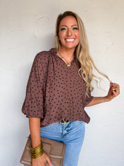 Lisa modeling the Umgee Save Me A Piece Polka Dot Chocolate Top, made from 80% rayon and 20% nylon, featuring dark polka dots, a ruffled split neckline, gathered shoulders, and sleeves extending below the elbows, styled with light-wash wide-leg jeans, black pointed-toe shoes, gold-tone jewelry, and a taupe handbag