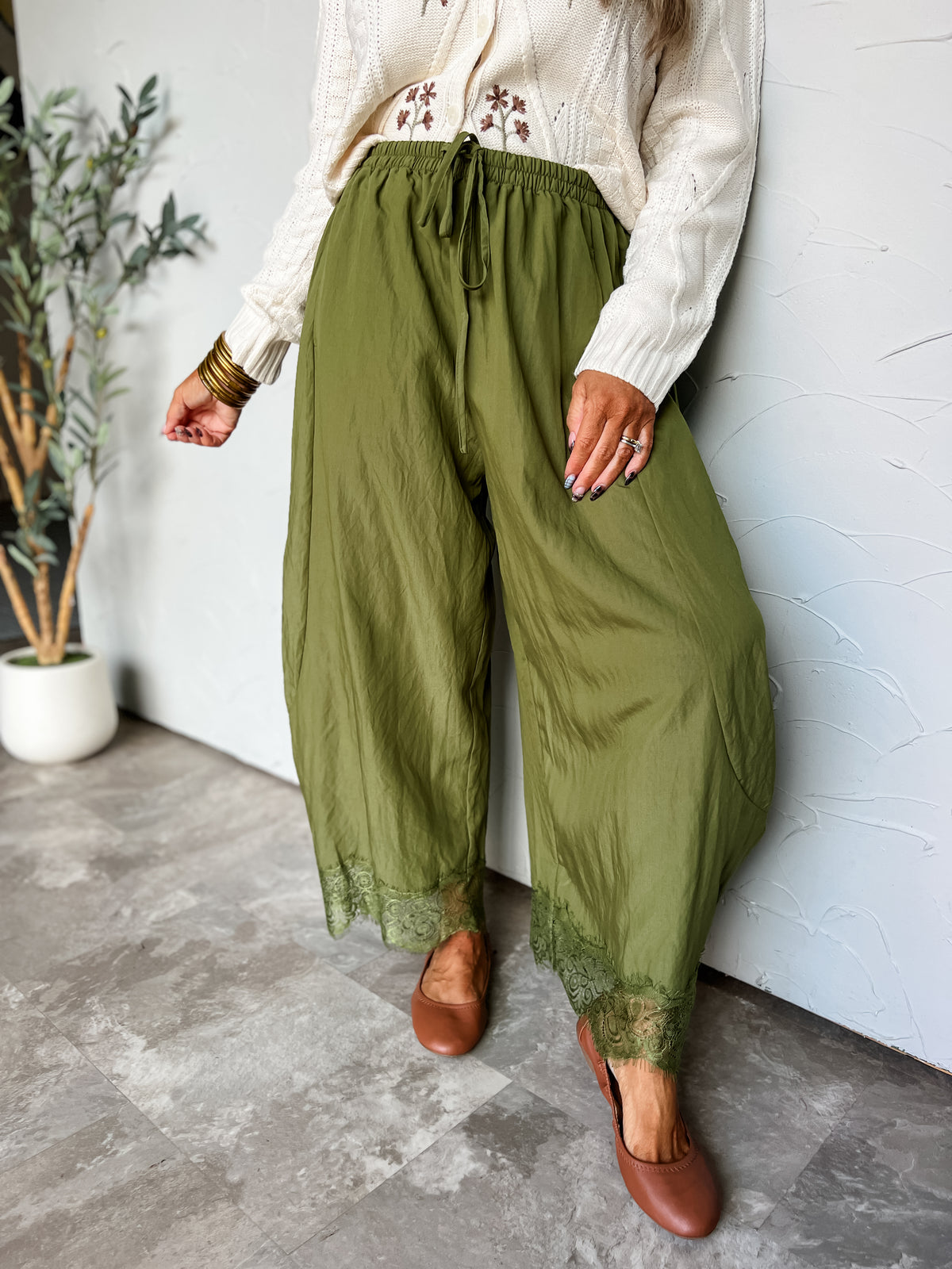 Lesly modeling BON Stay Here Balloon Leg Delicate Lace Pants in Fall Green, made from 85% rayon and 15% nylon, featuring a gathered drawstring waistband, balloon-shaped legs, and scalloped lace-trimmed hems, styled with a cream embroidered blouse and brown flats.