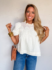 Lisa modeling the Entro A Lot To Accomplish Puff Sleeve Top in cream, made from 100% cotton with floral eyelet detailing, short puff sleeves, and a ruffled neckline, styled with blue wide-leg jeans, leopard-print pointed-toe shoes, and a saddle-colored crossbody bag