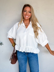 Lisa wearing the It’s My Attitude Striped Ruffle Shirt Button Down Top in white, size Large, made from 100% polyester with tonal stripe texture, a collared neckline, button front, voluminous elbow-length sleeves, gathered cuffs, and a ruffle hem, styled with cuffed jeans, leopard-print shoes, a brown handbag, and gold jewelry.