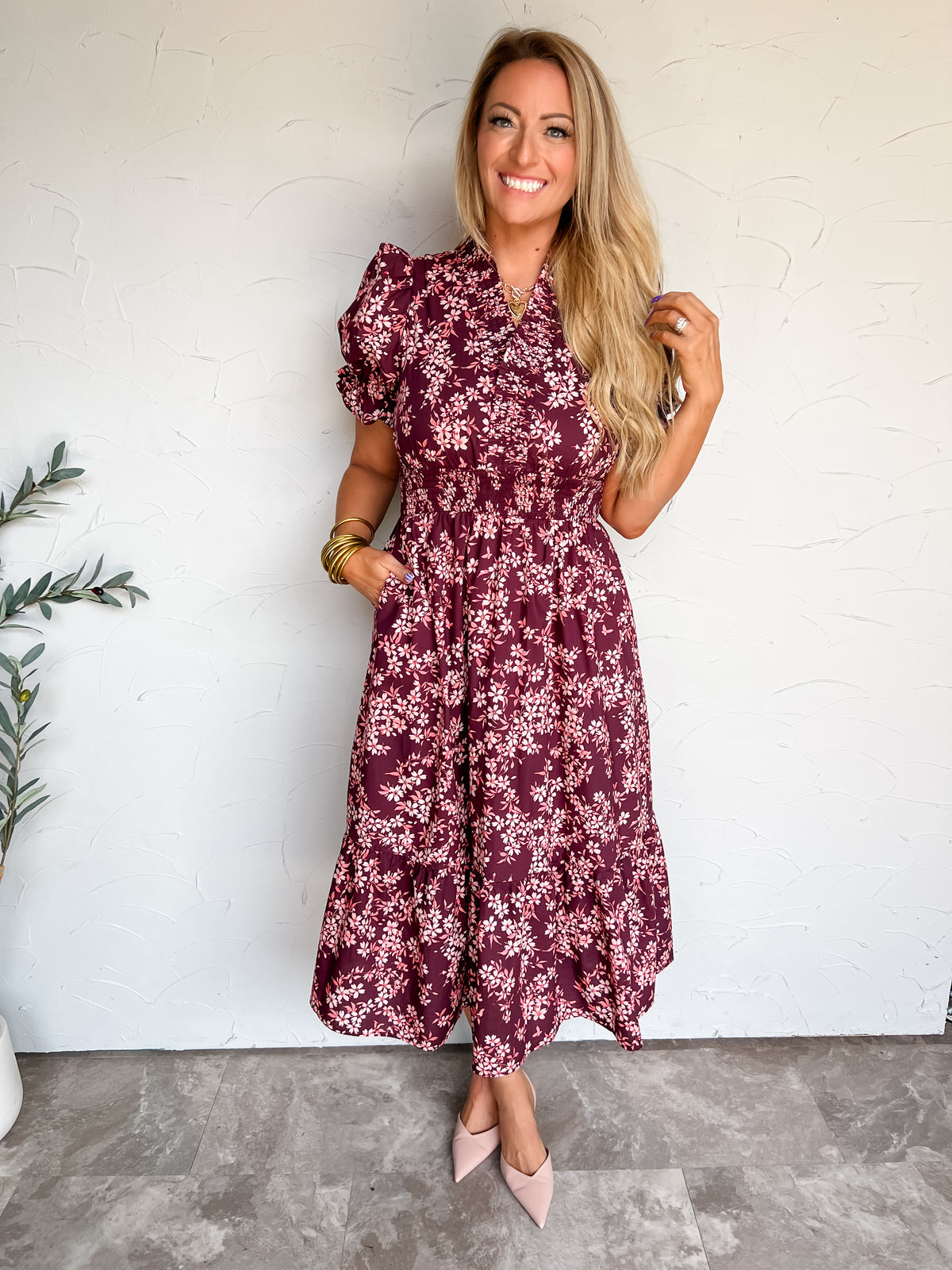 Lisa modeling the Entro Inspired By You Midi Dress, made from 100% cotton, with a burgundy background, light floral print, short puff sleeves, gathered waist, and side pockets, styled with pale pink pointed-toe heels and gold-tone jewelry.