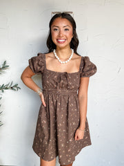 Happiness Ahead Floral Square Neck Mini Dress in dark brown by Blu Pepper, made of 100% cotton with small cream and pink florals, puff sleeves, and a front neckline tie.