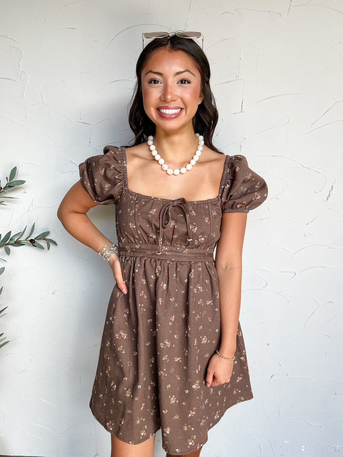 Happiness Ahead Floral Square Neck Mini Dress in dark brown by Blu Pepper, made of 100% cotton with small cream and pink florals, puff sleeves, and a front neckline tie.