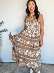 The Way She Looks Floral Tiered Dress by Blu Pepper in 100% polyester, with cream florals on a taupe-brown background, slim straps, a tiered skirt, and a smocked back.

