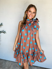 Never Leave You Polka Dot Tie Neck Mini Dress by Glam in 100% polyester, with turquoise dots on warm brown fabric, a side neck bow, sleeveless styling, and a ruffled hem.