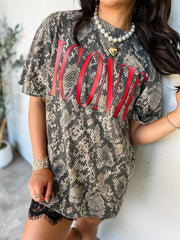 A woman wearing an oversized short-sleeve t-shirt with a gray and beige snakeskin pattern and large red 'ICONIC' text across the chest, styled with black lace shorts and gold jewelry.