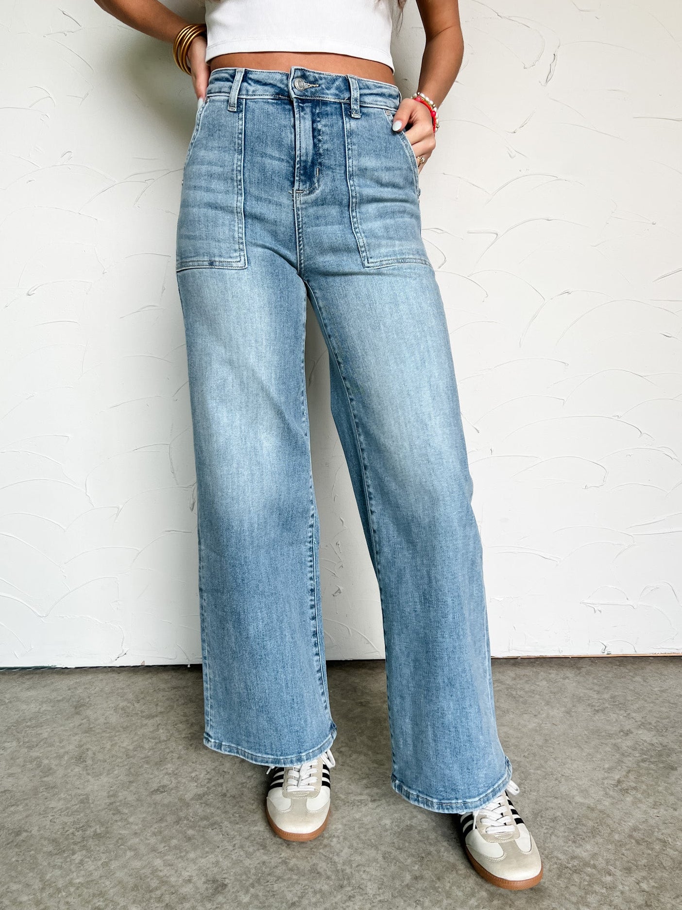 Person wearing light blue jeans and white sneakers against a plain background