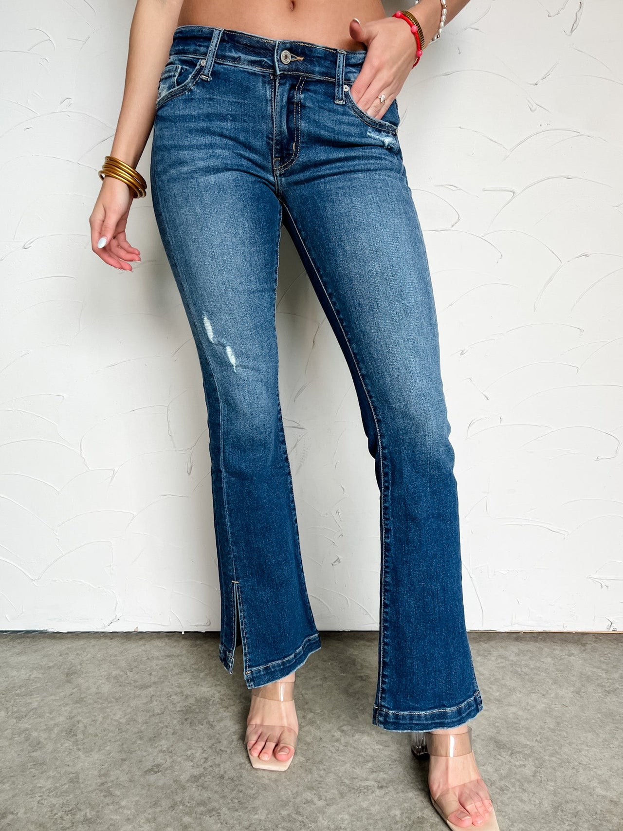 Person wearing low rise boot cut  blue jeans against a white brick wall.