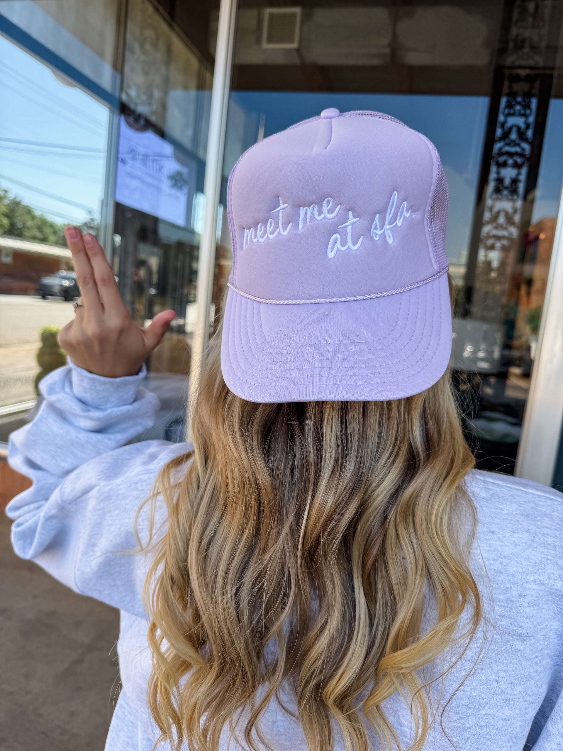 Person wearing a lavender cap with text, standing outside a building.