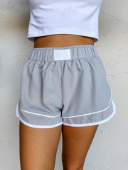 Girl in grey shorts in front of plain wall 