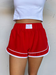Red shorts with white trim worn by a person against a light background