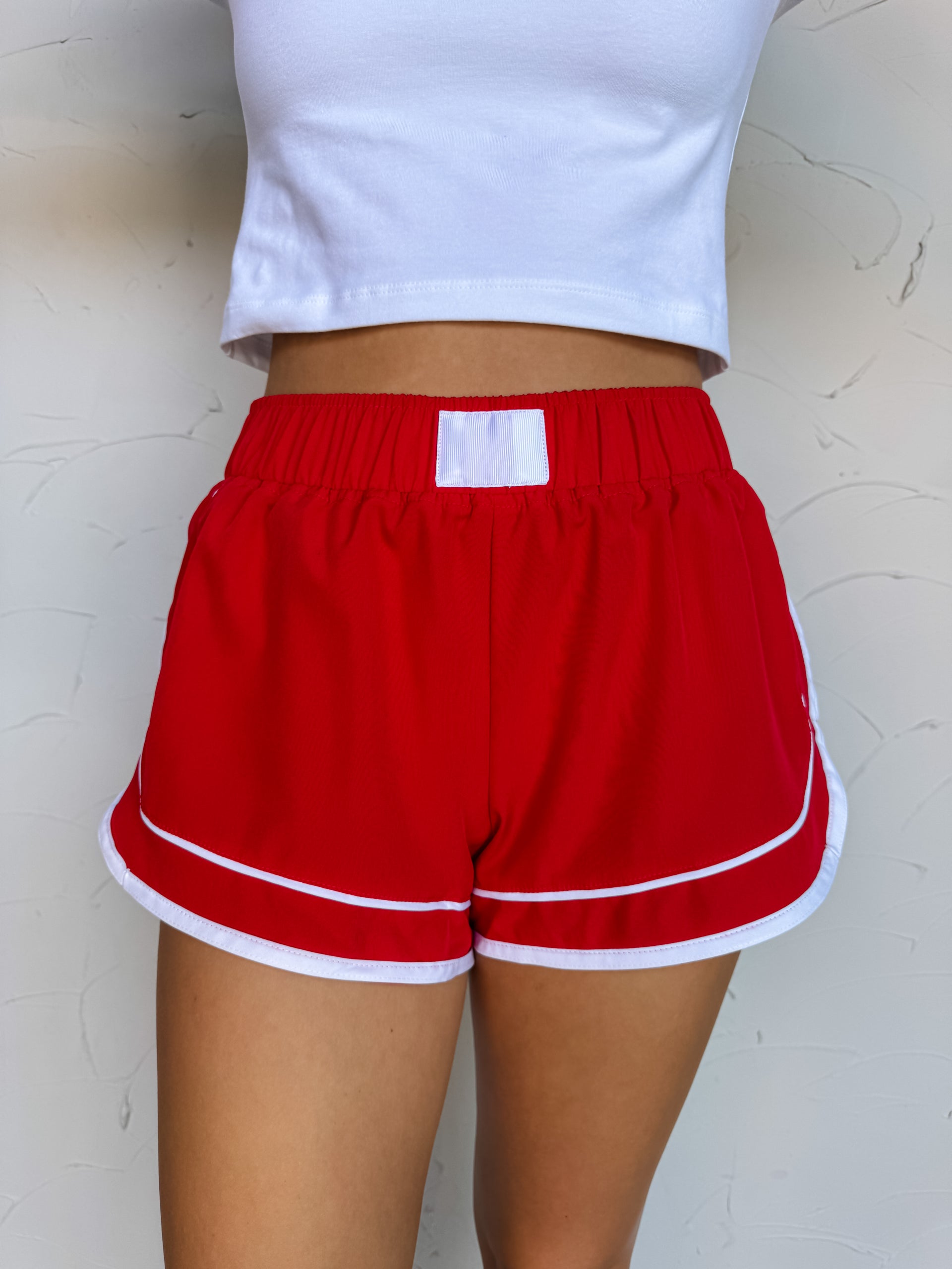 Red shorts with white trim worn by a person against a light background