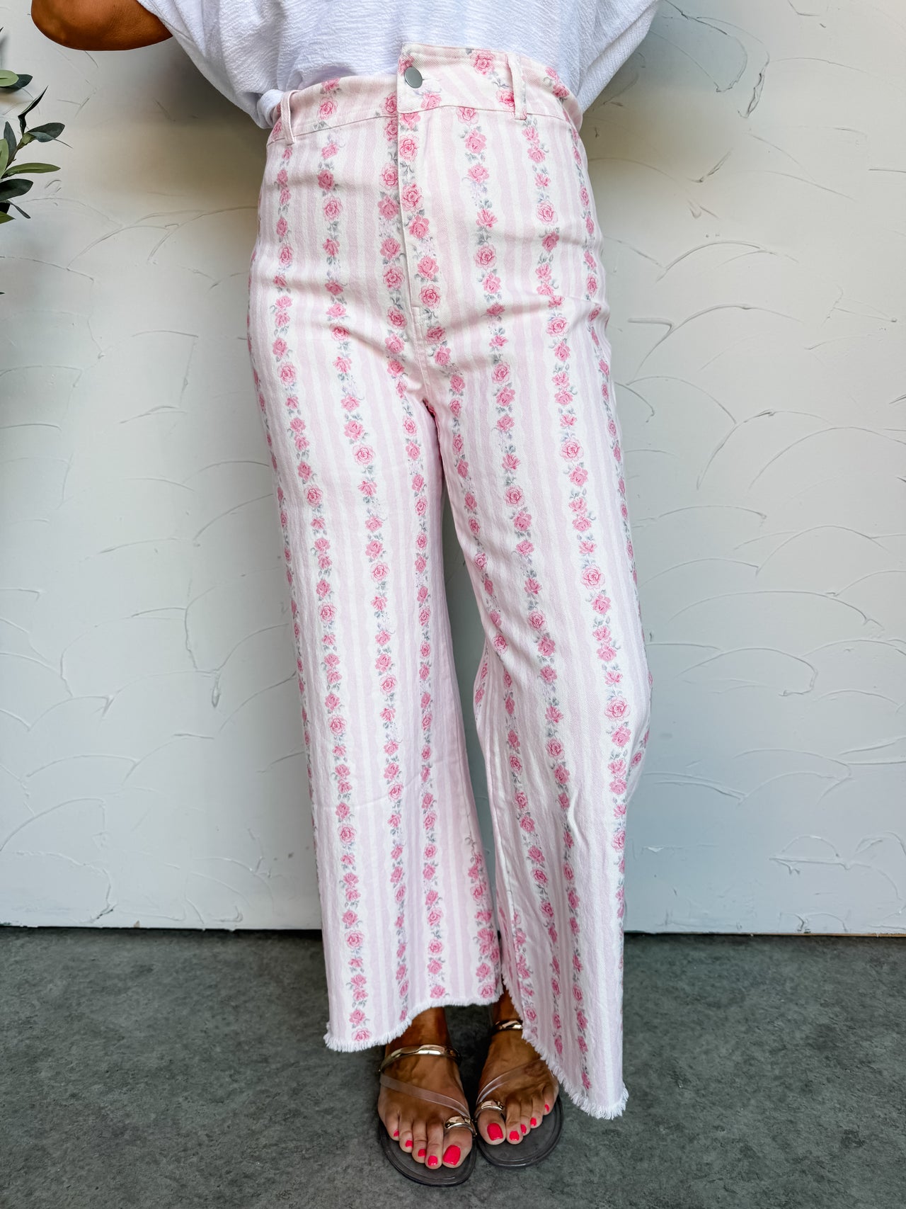 Person wearing white pants with pink floral pattern against a white wall.