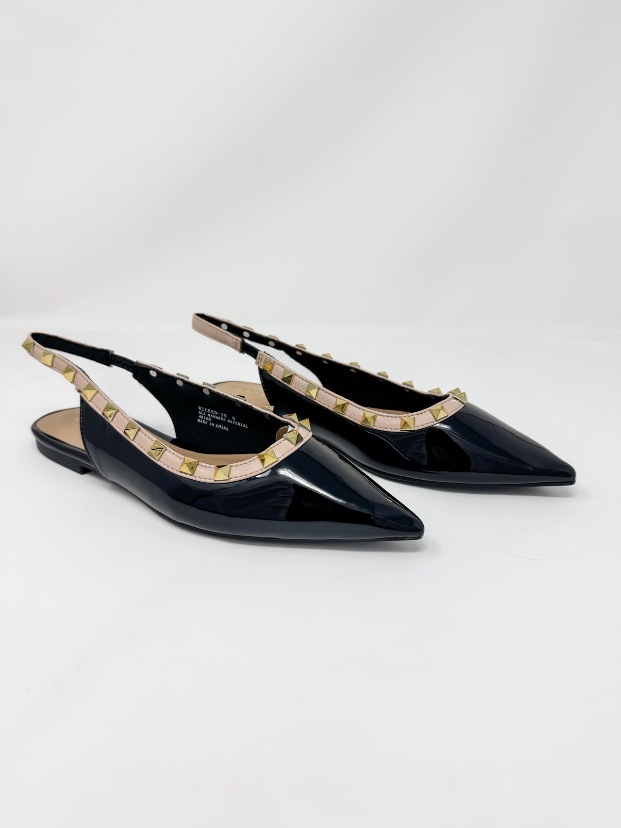 A pair of black patent leather slingback pointed-toe flats decorated with gold-tone studs along the strap, shown on a light gray studio background.