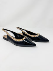 A pair of black patent leather slingback pointed-toe flats decorated with gold-tone studs along the strap, shown on a light gray studio background.