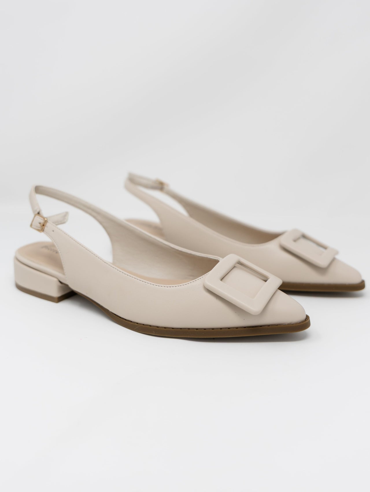 A pair of Pierre Dumas cream-colored pointed-toe slingback flats displayed against a solid white background. The shoes feature an adjustable ankle strap with a small gold buckle, a very low block heel, and a large matching cream square buckle detail across the pointed toe.