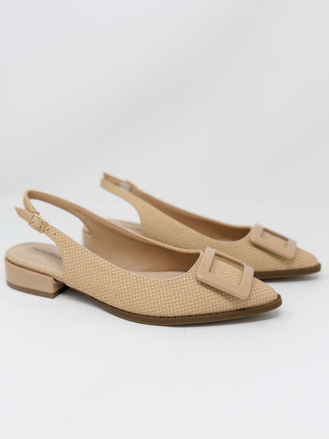 A pair of Pierre Dumas tan woven raffia pointed-toe slingback flats displayed against a solid white background. The shoes feature an adjustable ankle strap with a small gold buckle, a low block heel, and a large smooth tan square buckle detail across the toe box.